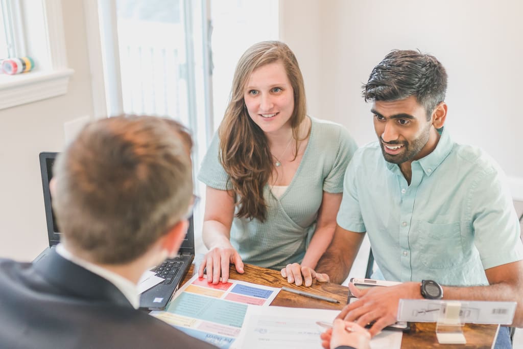 Two owners meeting their property manager across a table with a laptop and samples