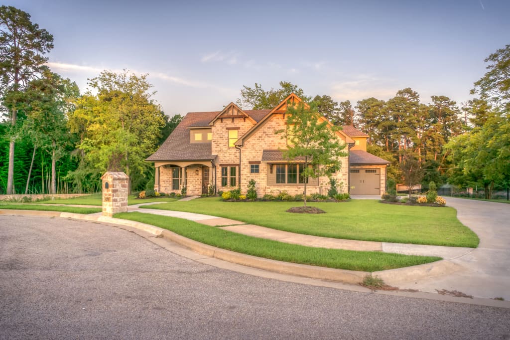 Stone-fronted house at the end of a long driveway, framed by mature trees